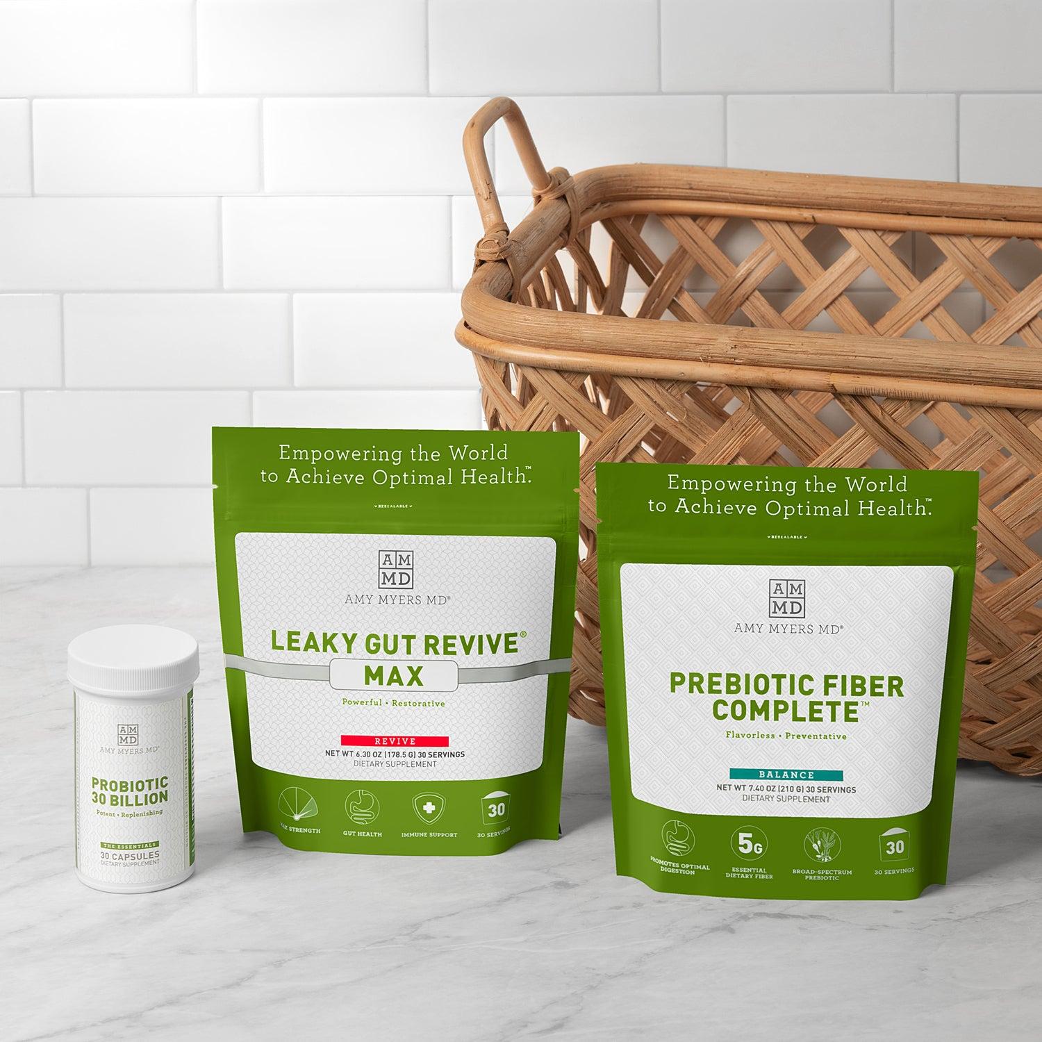 Picture of the Everyday Gut Health Kit on a grey marble counter top in front of a house plant and white wall. The products featured in the kit are presented with the AMMD Prebiotic Fiber Complete next to AMMD Leaky Gut Revive Max, both featured in vibrant Green resealable bags, positioned in back of the white AMMD Probiotic 30 Billion , 30 capsule pill bottle.