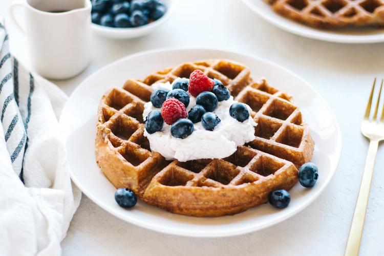 Belgian waffle with butter in the center and blueberries and raspberries on top plated nicely.