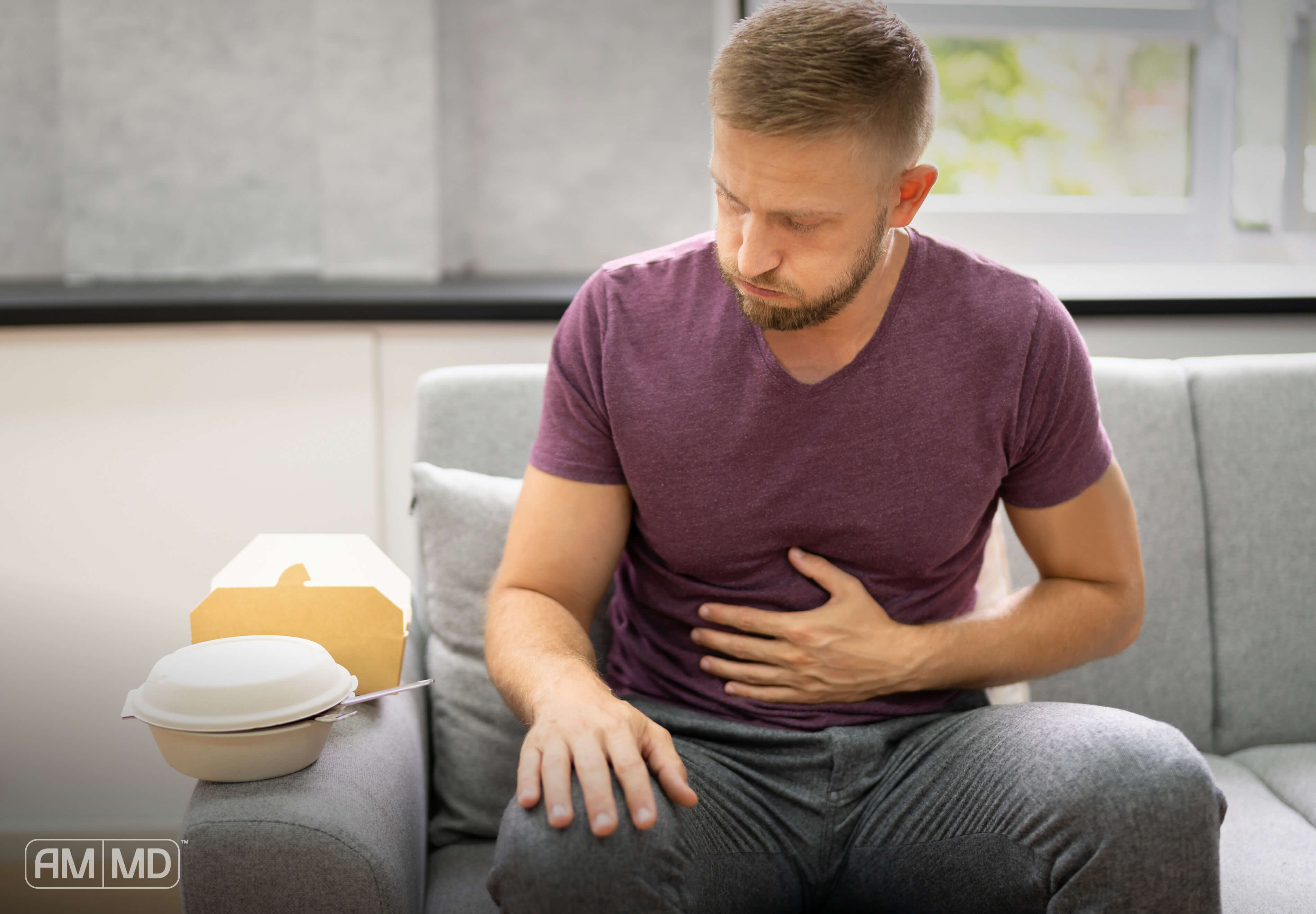 Man holding his stomach sitting on the couch. Article The Benefits of Gut Restore with Betaine HCL for Digestion