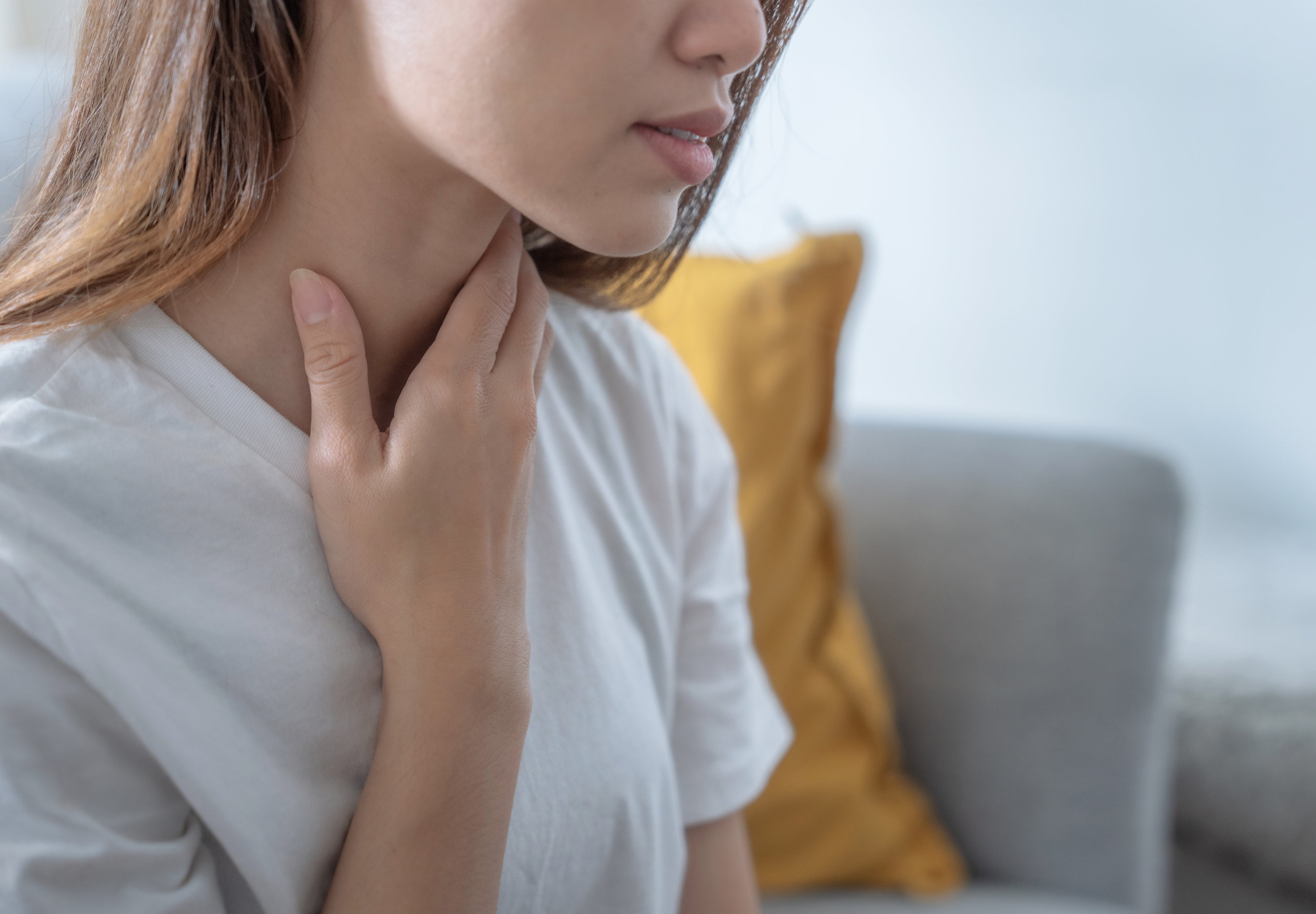   Woman touching her throat to illustrate thyroid dysfunction, hypothyroidism symptoms, and hormone imbalance