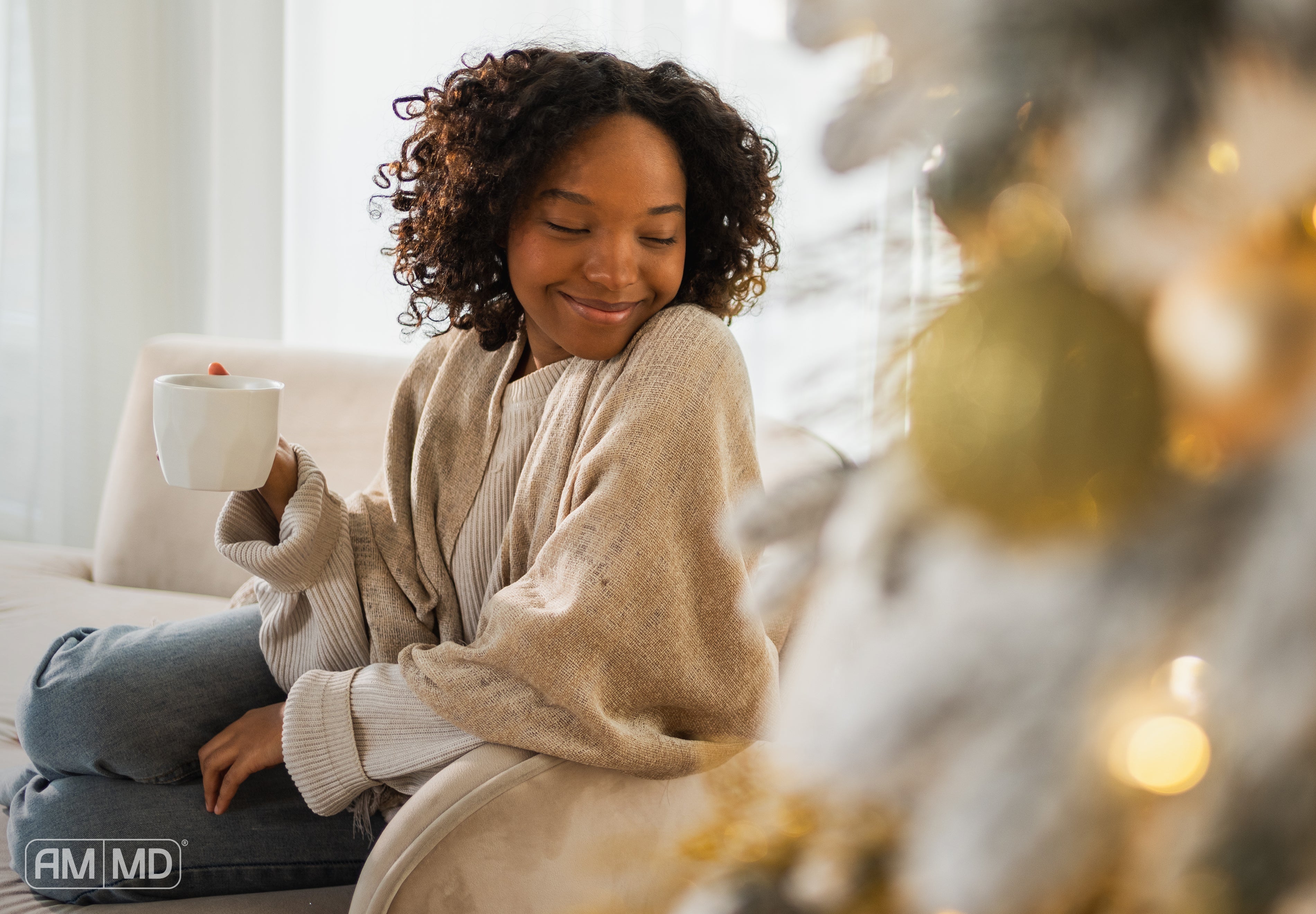Woman sitting by christmas tree enjoying tea - Holiday Recovery: How to Restore Your Energy and Wellness - AMMD™