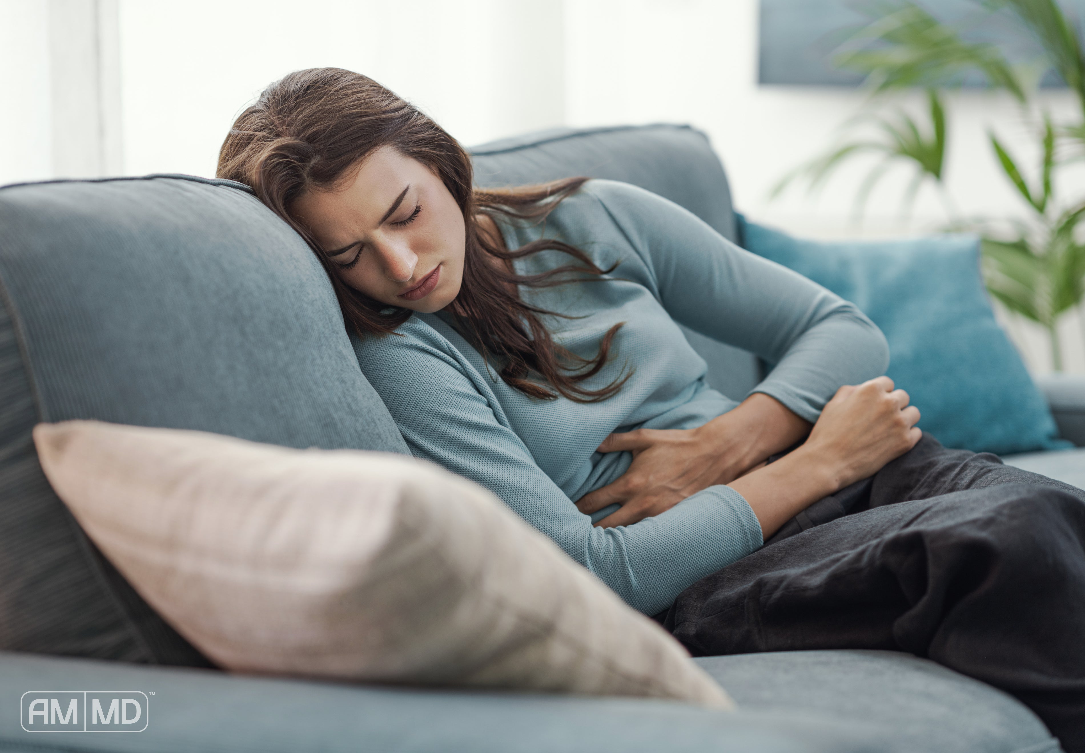 Woman laying on the couch holding her stomach - How Biofilm in Your Gut Disrupts Digestive Health - AMMD™