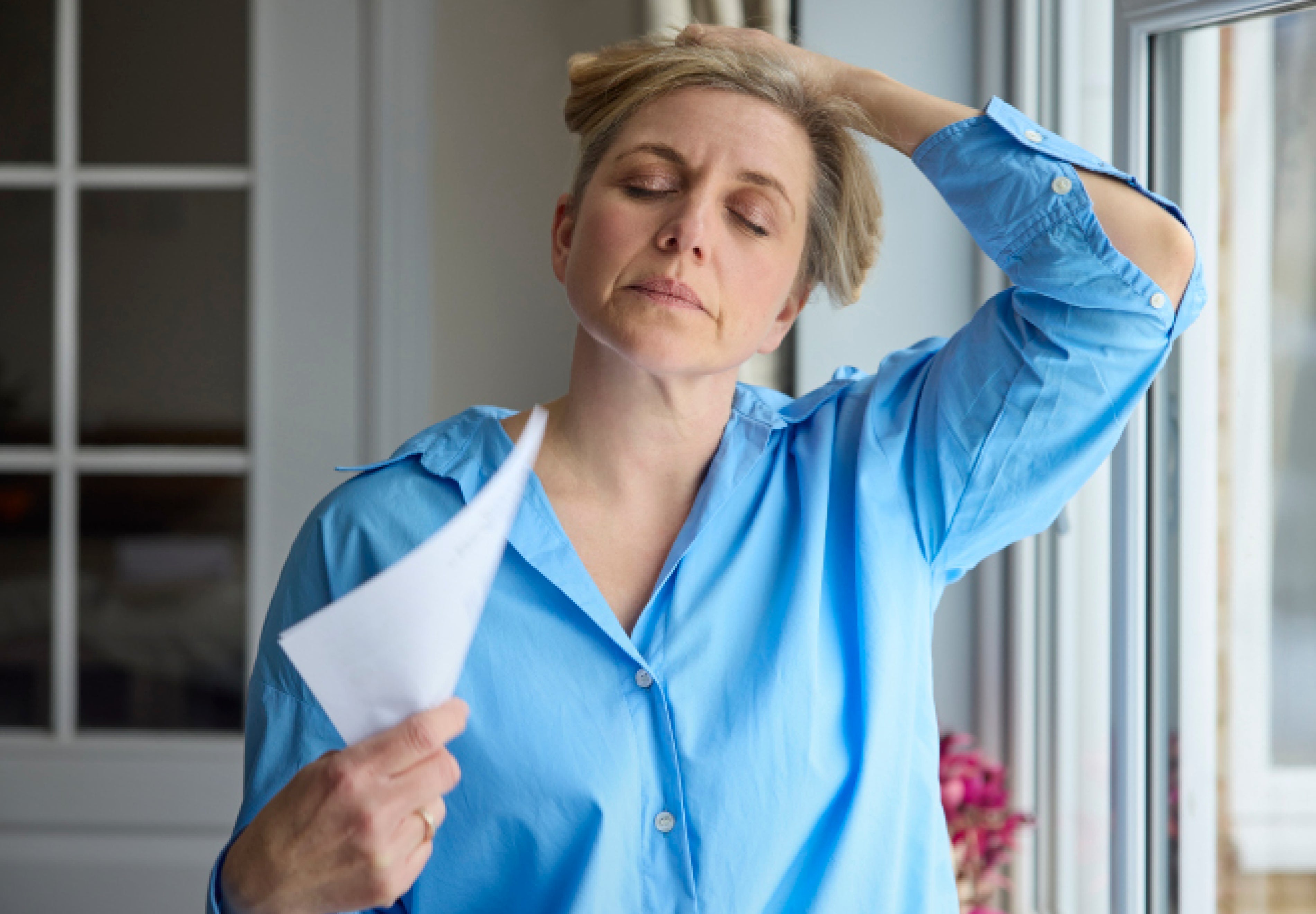 woman experiencing hot flashes and overheating during perimenopause, fanning herself by a window
