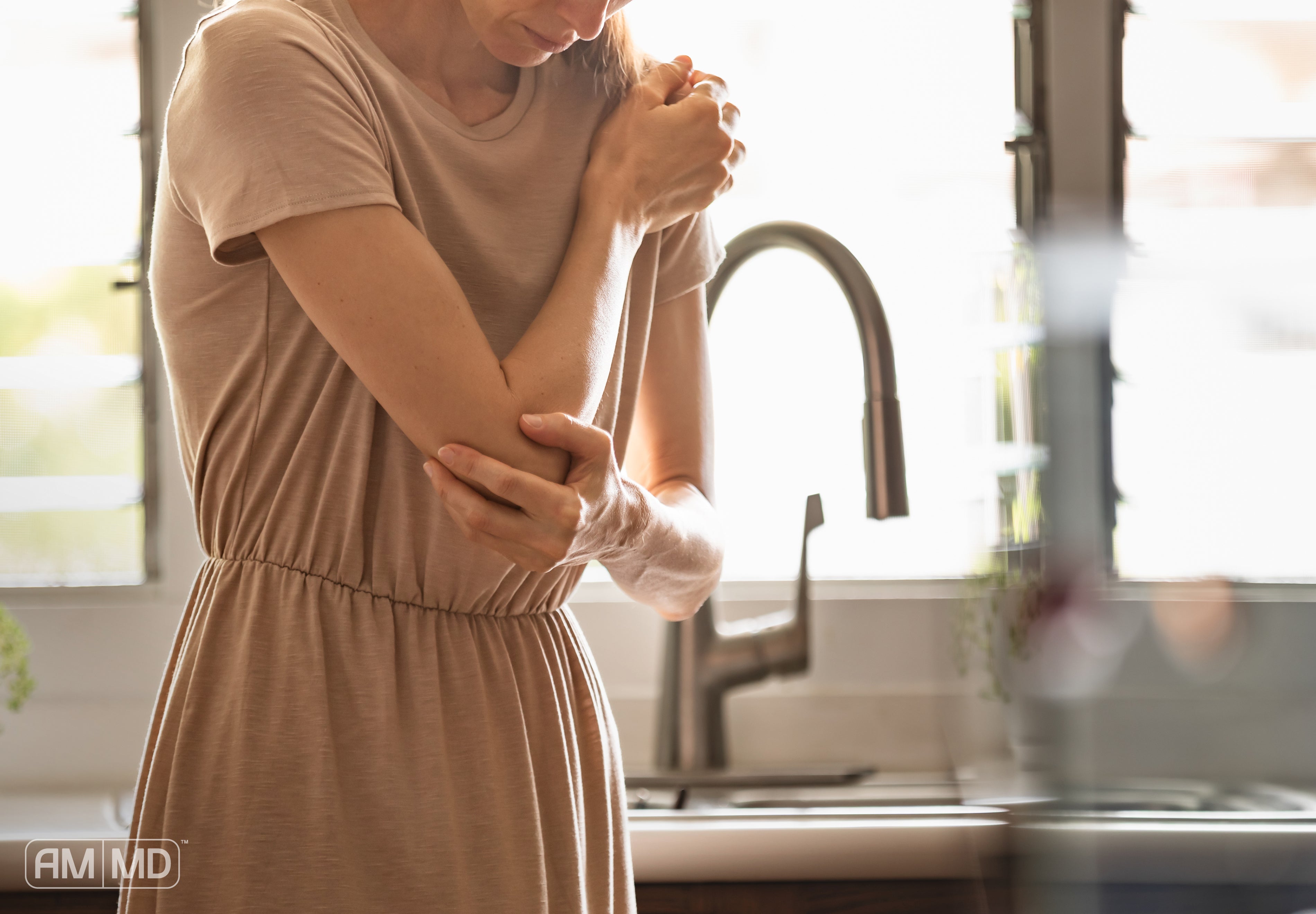 Woman rubbing elbow in pain - Perimenopause and Autoimmune Disease Flares: What’s the Link? - AMMD™