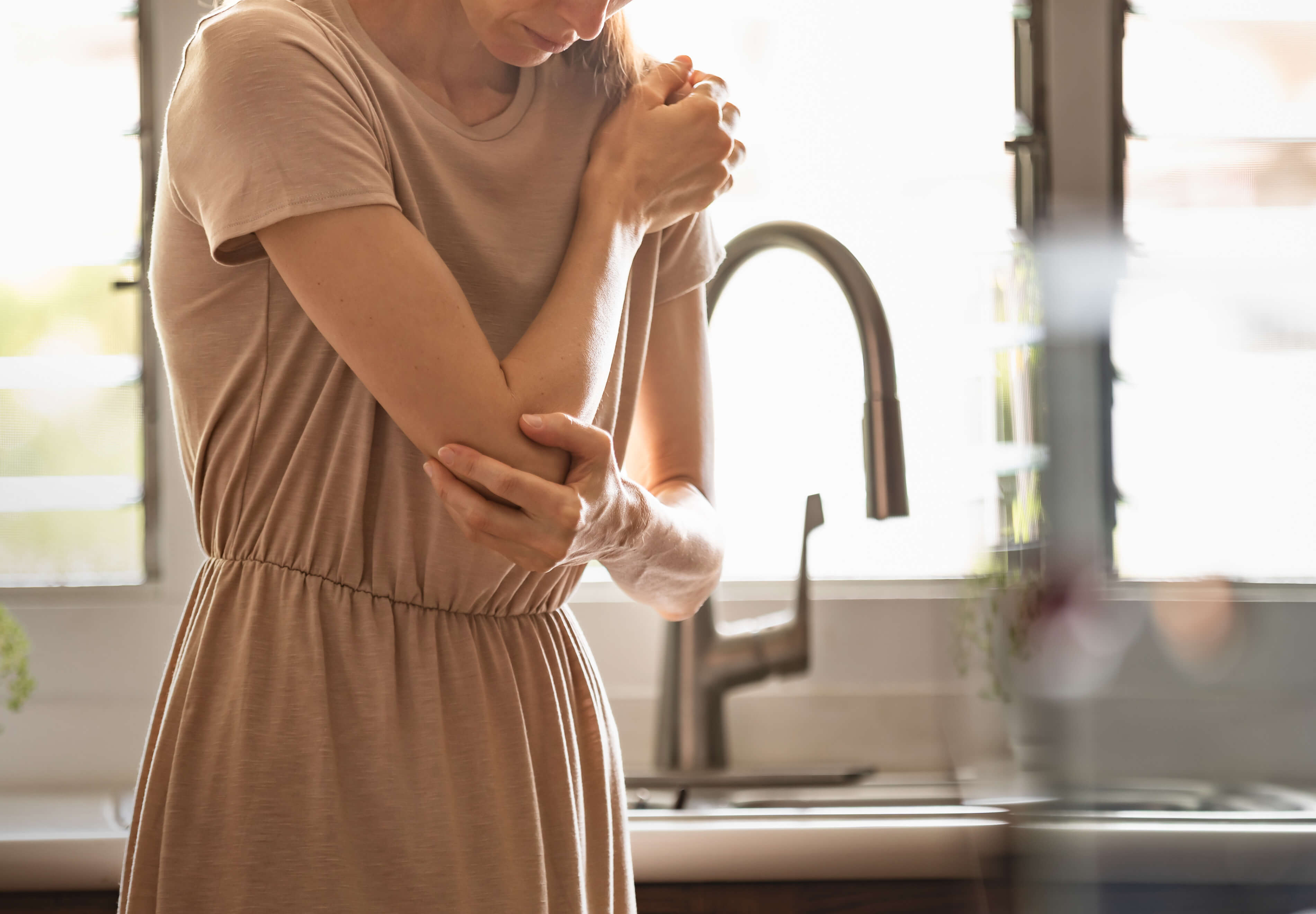 Woman rubbing elbow in pain - Perimenopause and Autoimmune Disease Flares: What’s the Link? - AMMD™