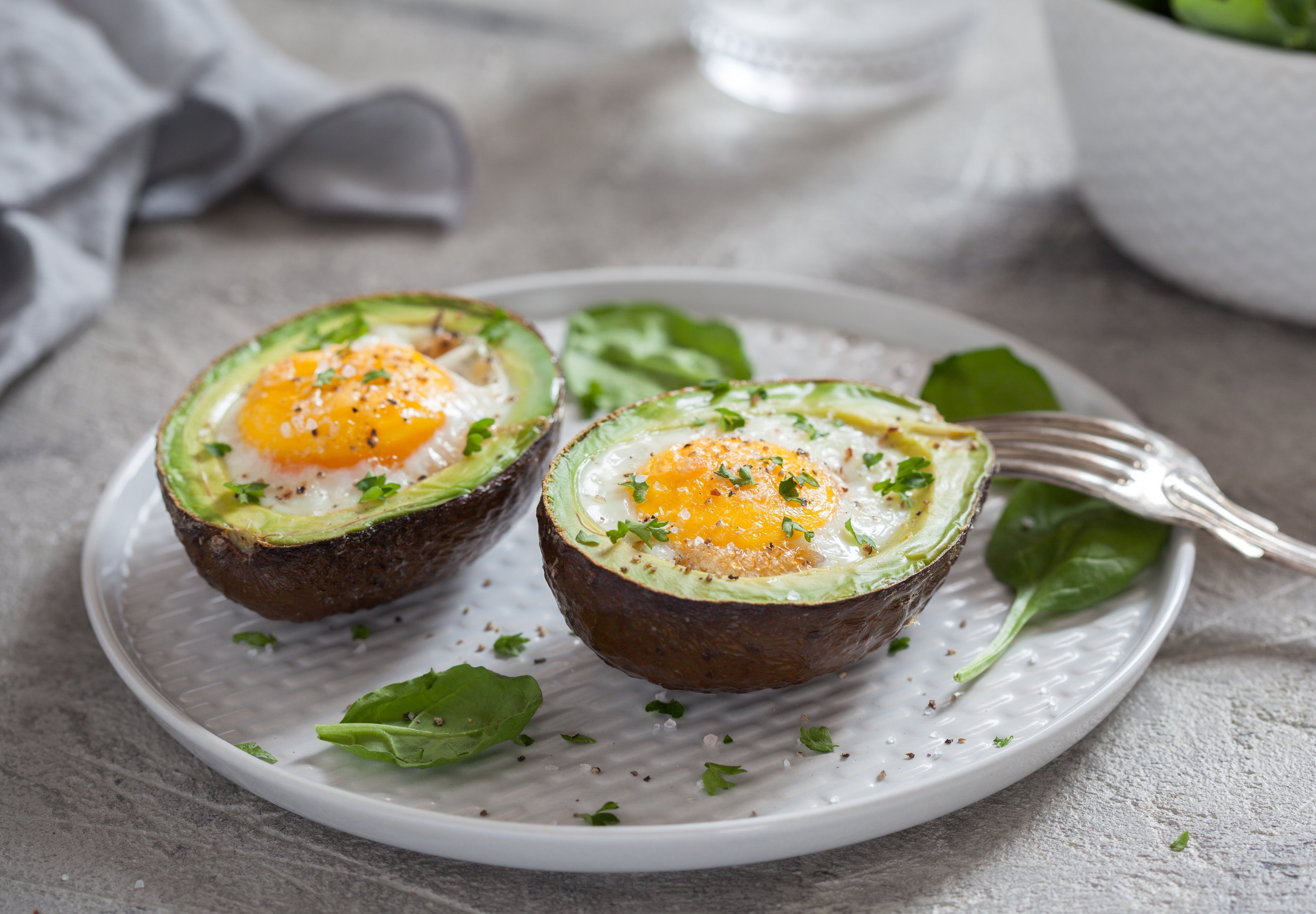 baked avocado eggs topped with herbs and sea salt on a white plate for a healthy keto breakfast