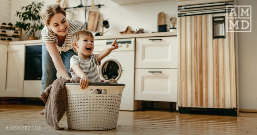 A mom pushes her young son around the kitchen in a laundry basket - The Autoimmune Spectrum - Amy Myers MD®