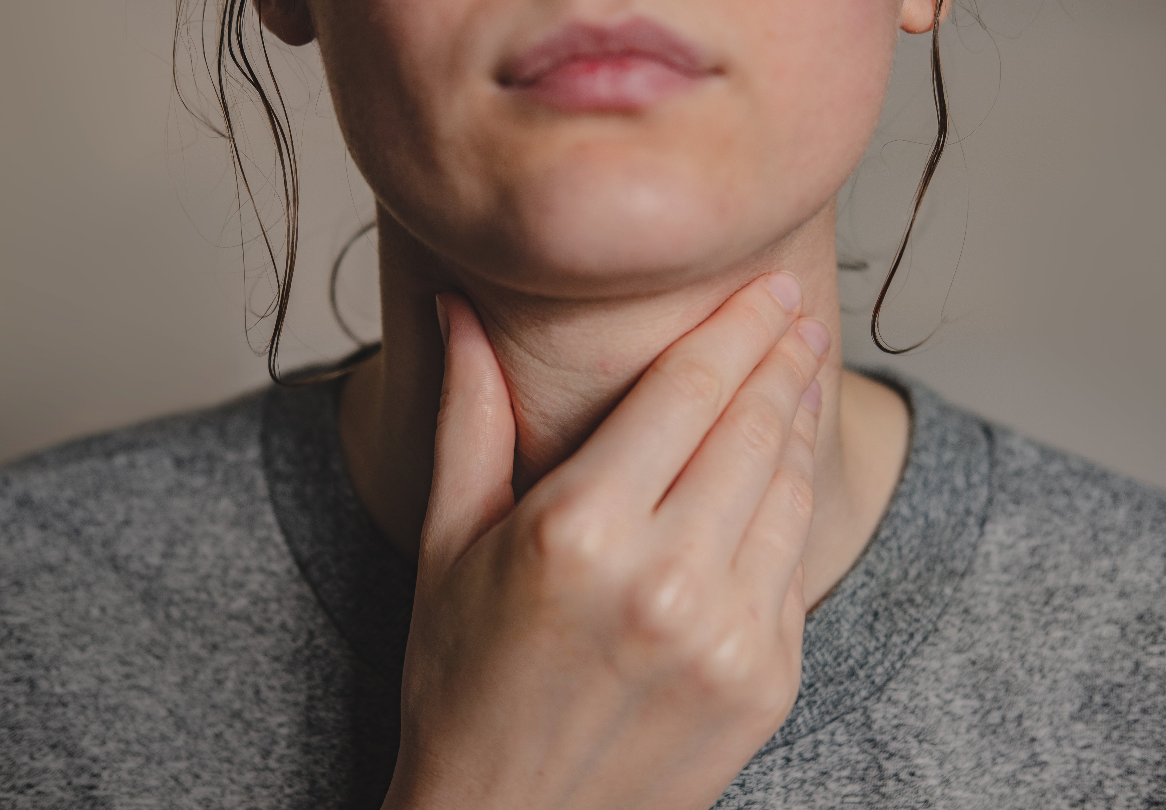 Woman touching her throat, representing the connection between SIBO, Hashimoto’s disease, gut health, and thyroid function.