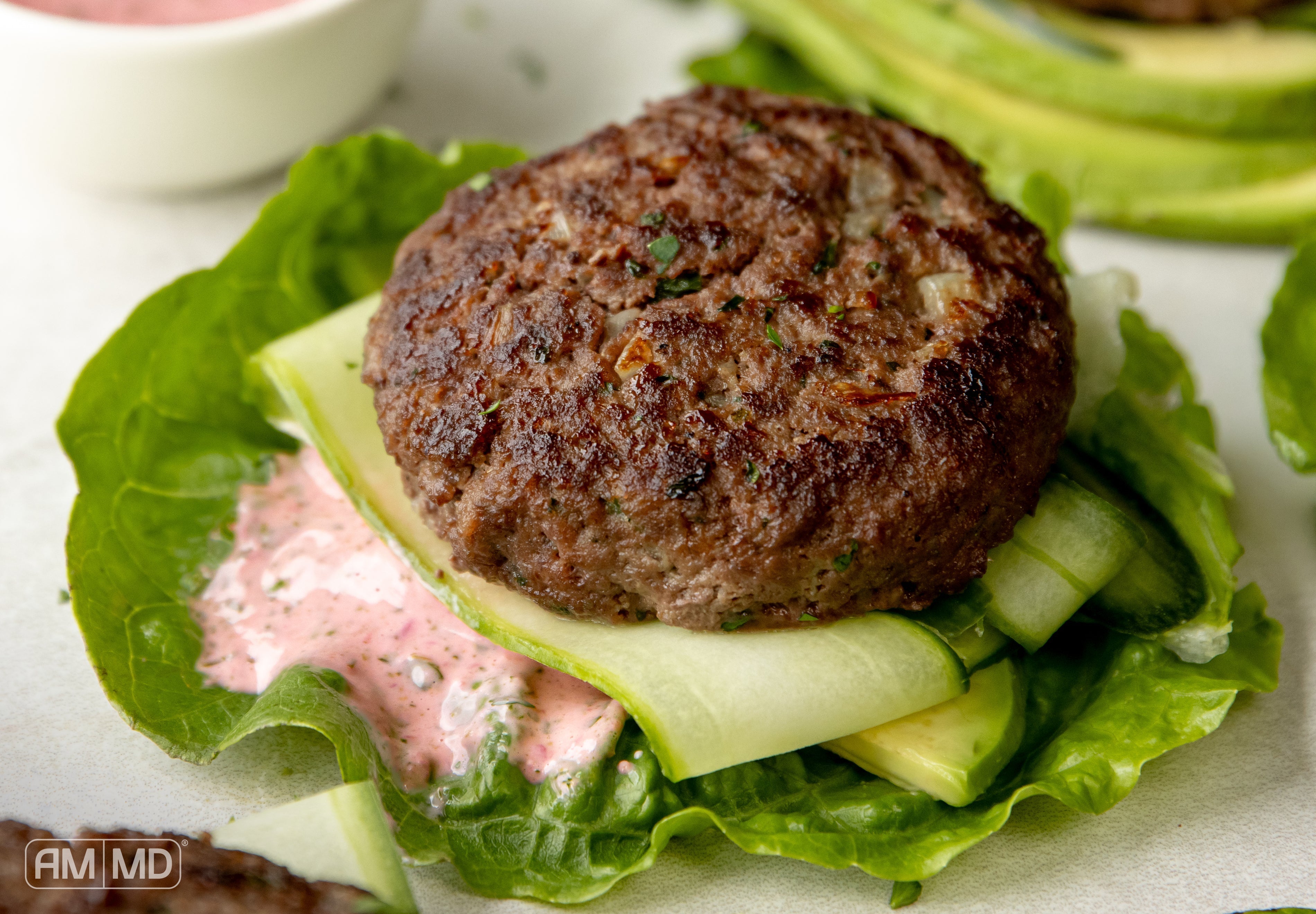 Gluten & dairy-free beef liver burger served in a lettuce wrap with avocado, cucumber ribbons, and pink sauce.
