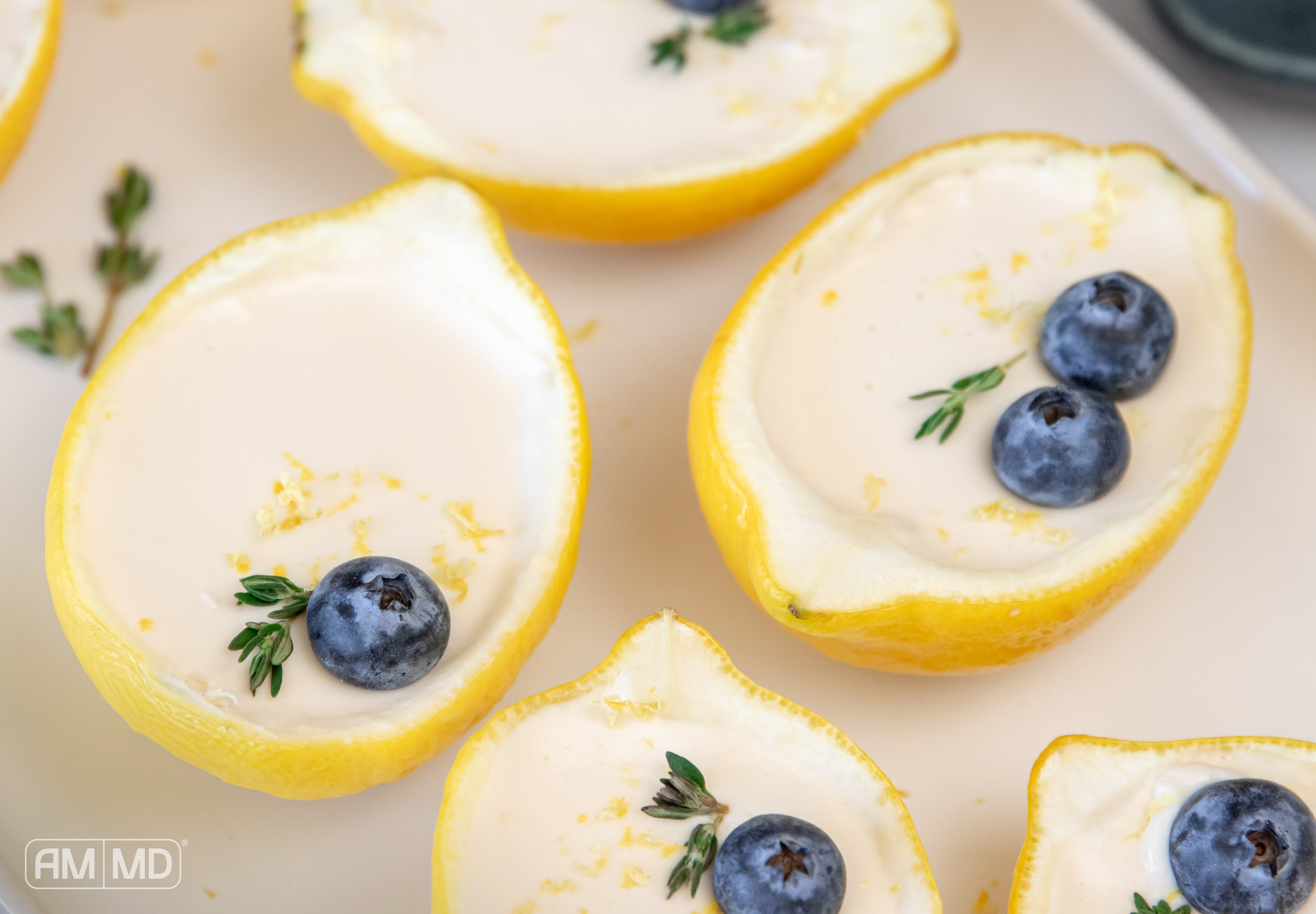 AIP lemon posset served in lemon halves, topped with blueberries and fresh herbs