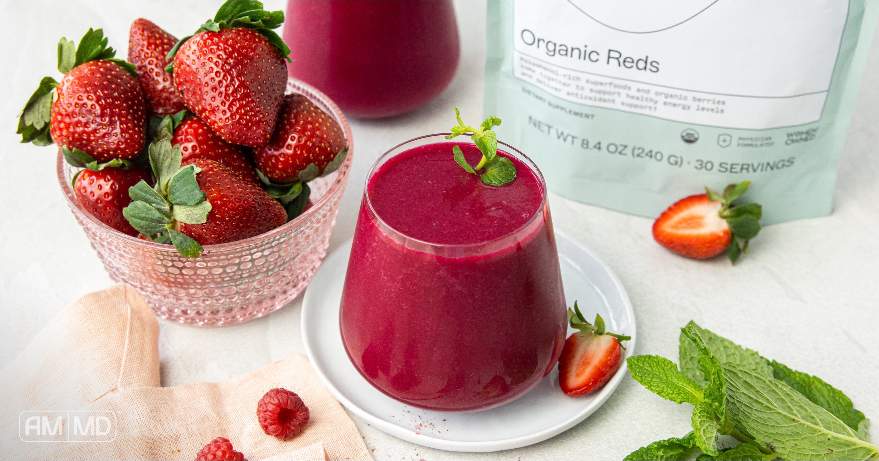 A glass of Organic Superfood Reds & Beet Smoothie next to a bowl of strawberries - AMMD™