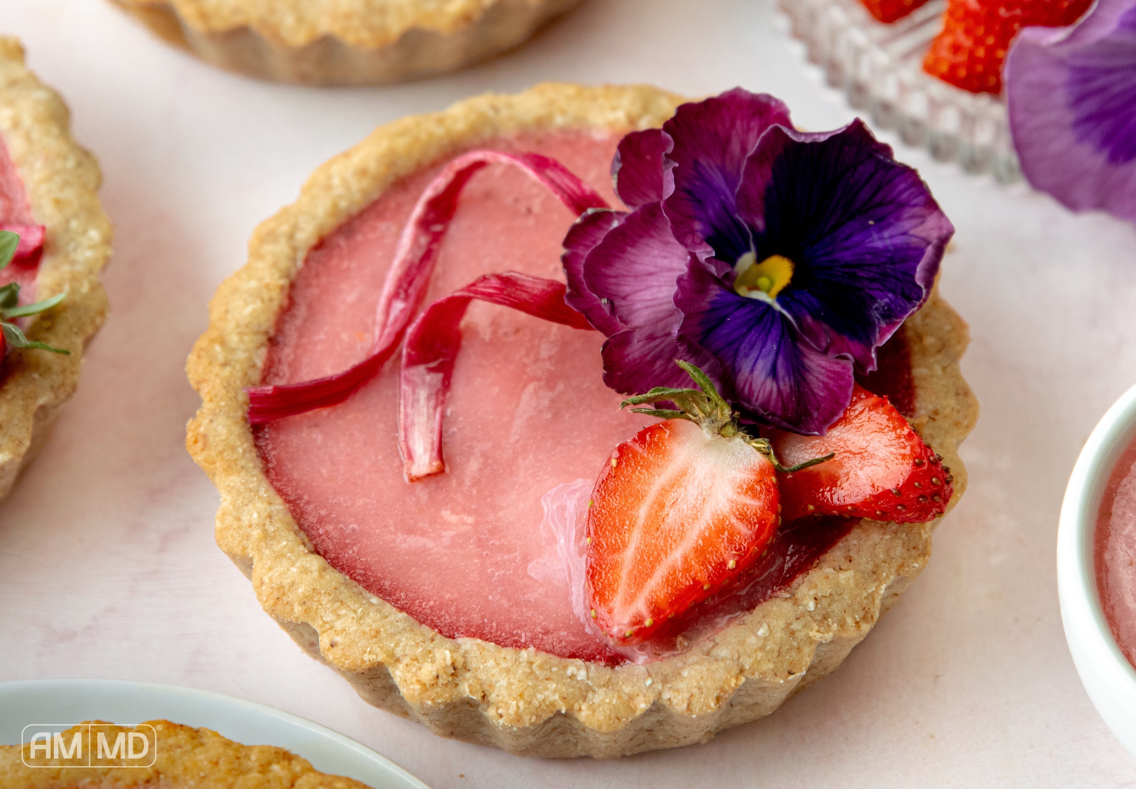 High-protein strawberry rhubarb tartlet with fresh strawberries and edible flower garnish