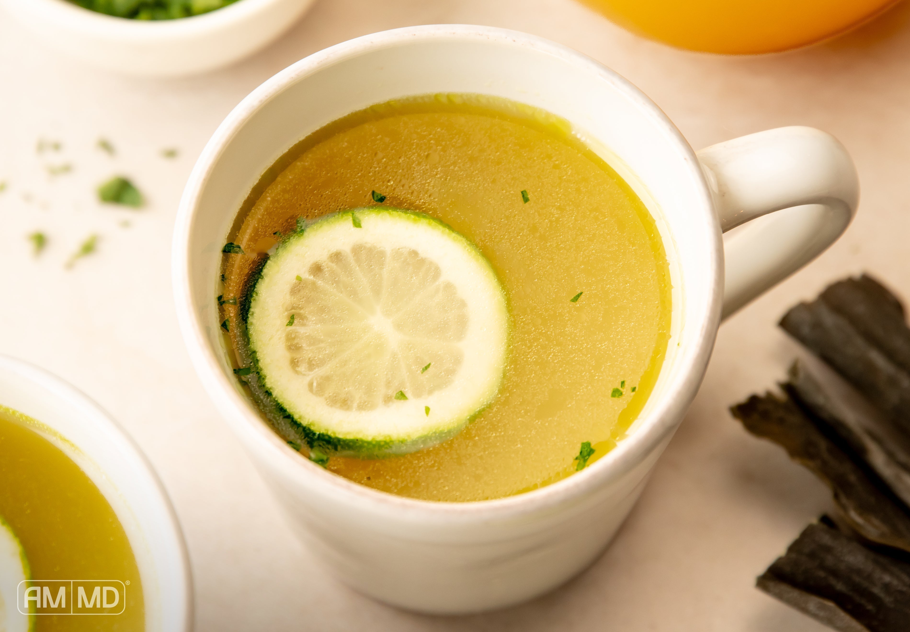 Mug of savory umami bone broth with lime and herbs for gut, thyroid, and immune wellness