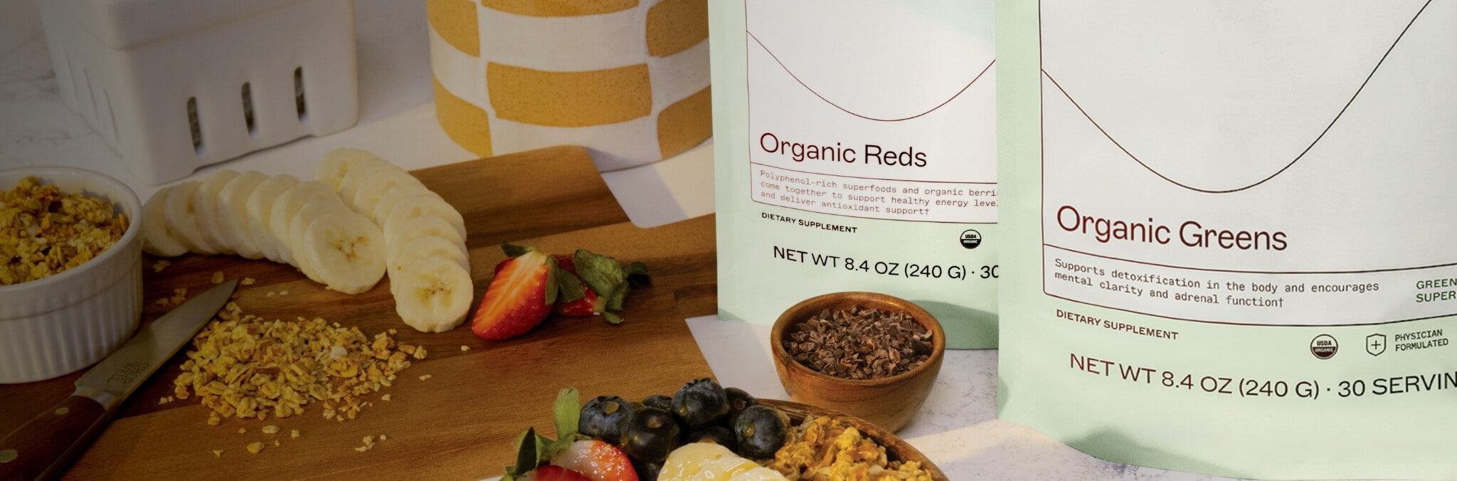 Daily Wellness Collection - Organic Reds and Organic Greens on a kitchen counter with a cutting board and fruits laying around