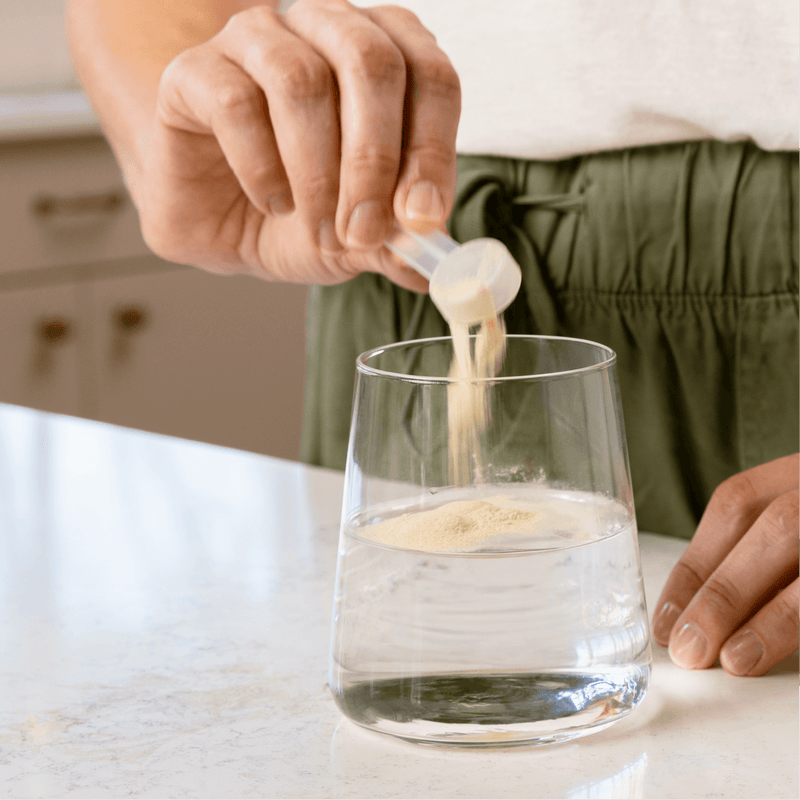 The Autoimmune Solution™ Protocol by AMMD background image of glass of water with leaky gut revive scoop pouring into water. 