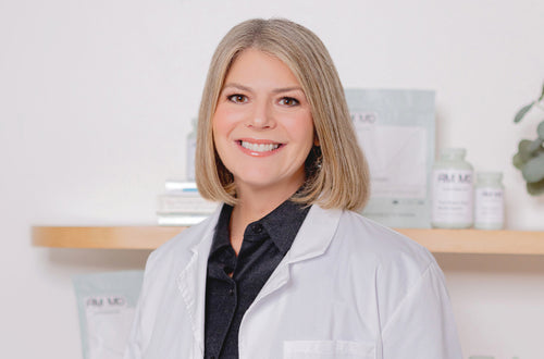Dr. Amy Myers smiling in a white lab coat, standing confidently against a simple, professional backdrop.