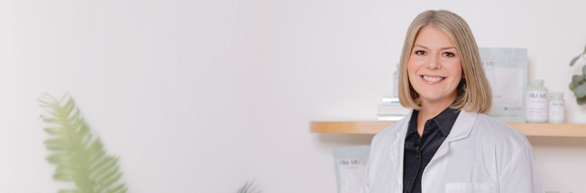 Dr. Amy Myers smiling in a white lab coat, standing confidently against a simple, professional backdrop.